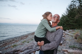 Girl planting a kiss on her grandfather’s cheek by the waterside.