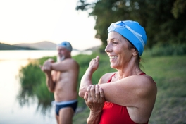 Deux nageurs portant un bonnet de natation s’étirent les bras en souriant avant de plonger à l’eau.