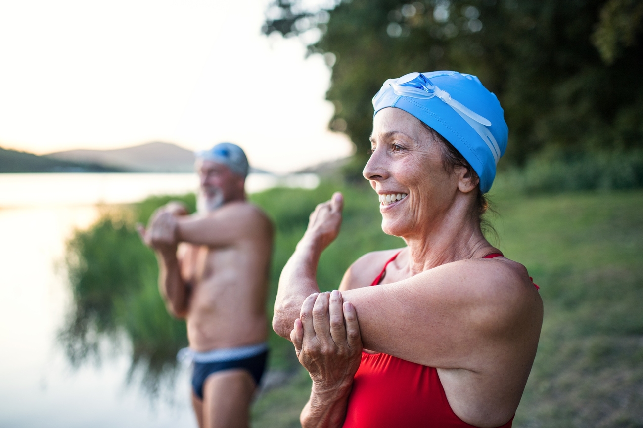 Two swimmers with pool caps stretching their arms and smiling before going in the water.