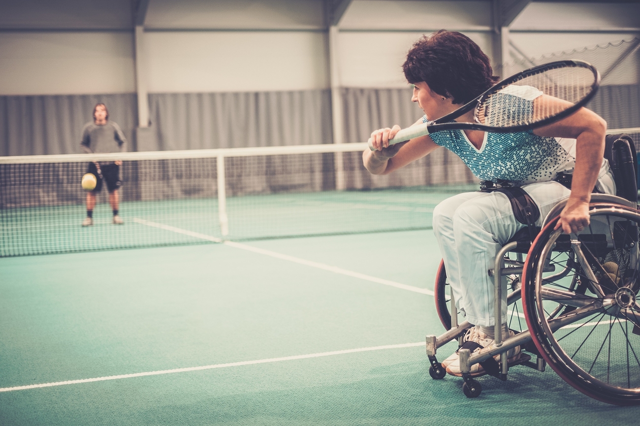 Person in wheelchair playing tennis against an able-bodied opponent.