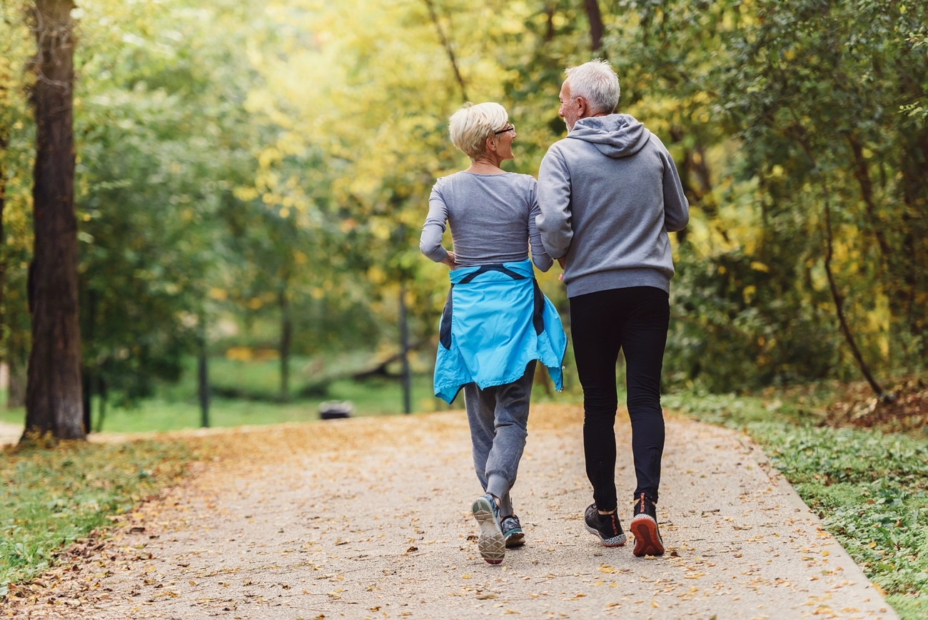 Older couple taking a stroll in autumn while wearing matching gray sweaters.