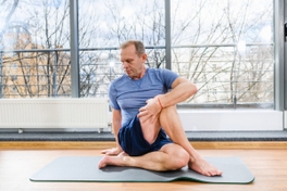 Man in yoga clothing doing a complex yoga pose at their studio on a mat.