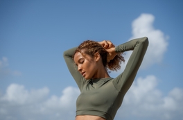 Woman in green athletic top stretching in front of blue sky.