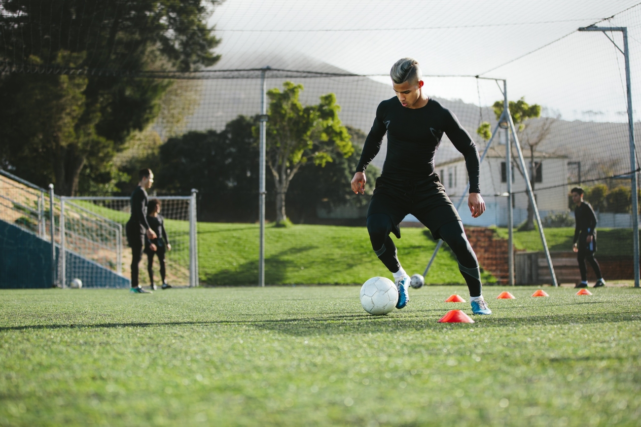 Soccer player wearing all black kicking his ball while warming up for a match.