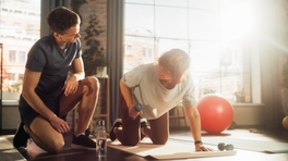 Personal trainer helping their client at a fitness studio as she lifts a small weight.