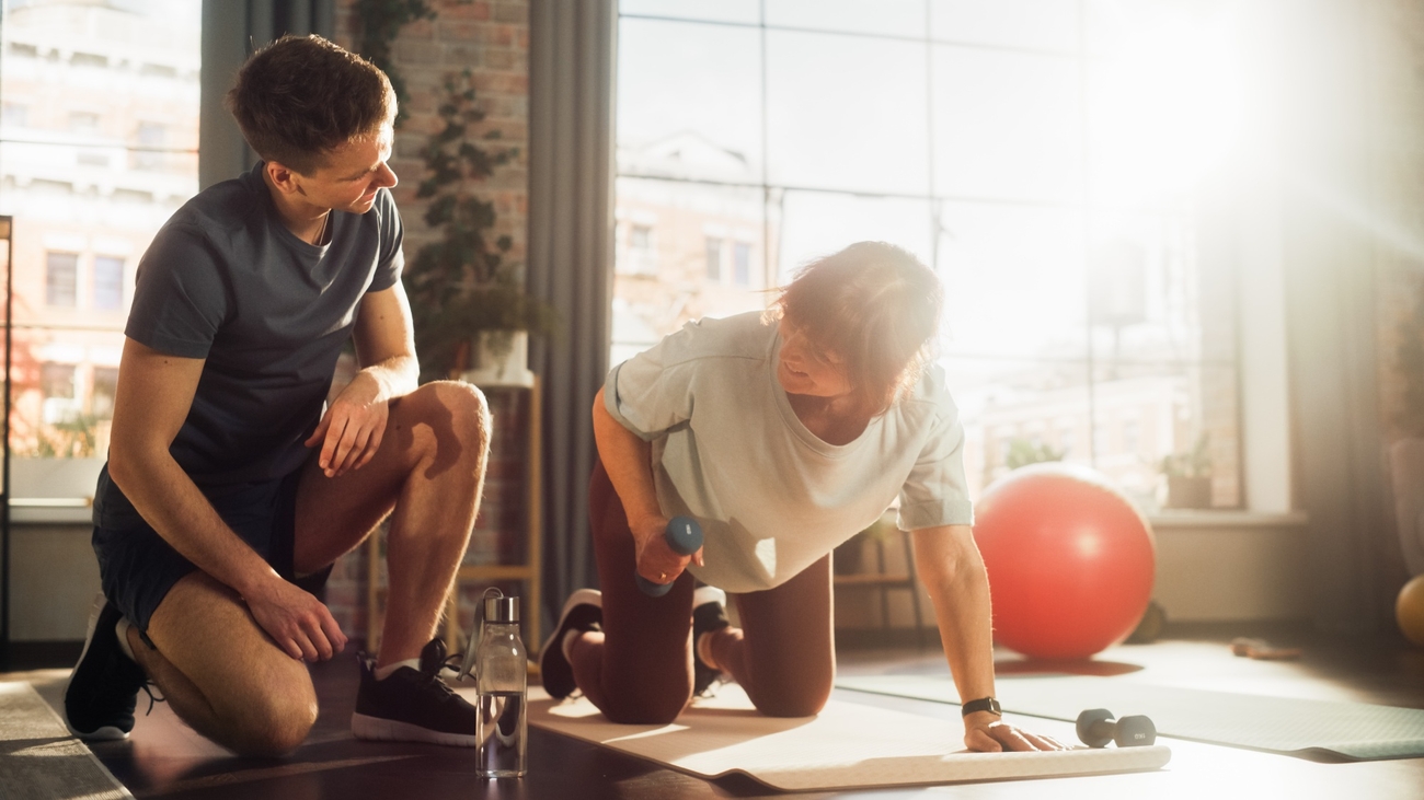 Personal trainer helping their client at a fitness studio as she lifts a small weight.