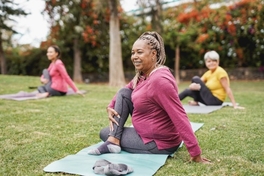 Three women smiling while practicing yoga at a public park.